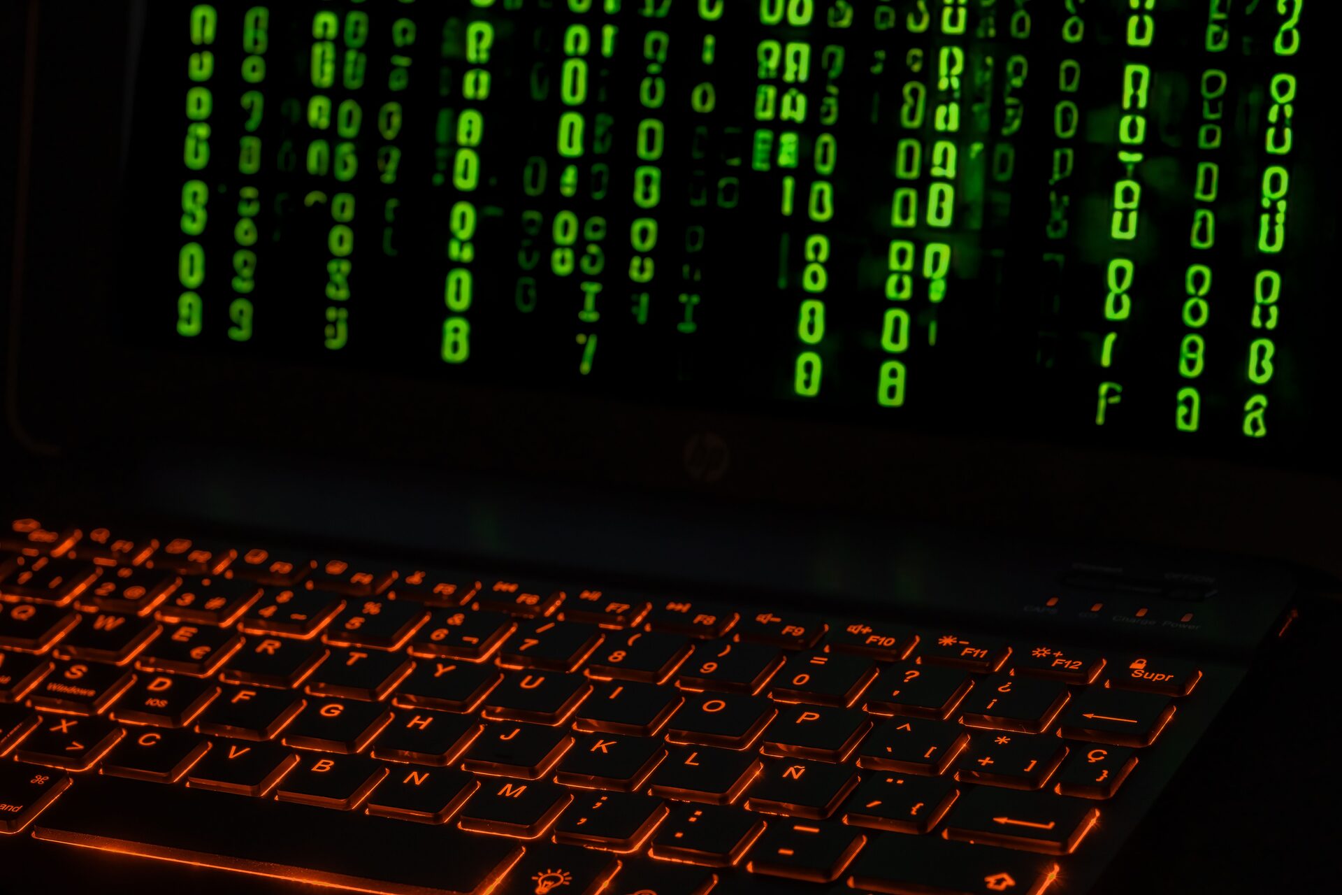 Close-up of a backlit keyboard with lines of code reflecting on the laptop screen